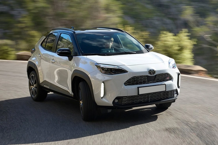 A white Toyota Yaris Cross driving along a country road.